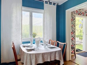 A dining area with a table set for four, a window with curtains, and a view of greenery outside. - Villa Stensborg by Interhome (Östra Ryd)