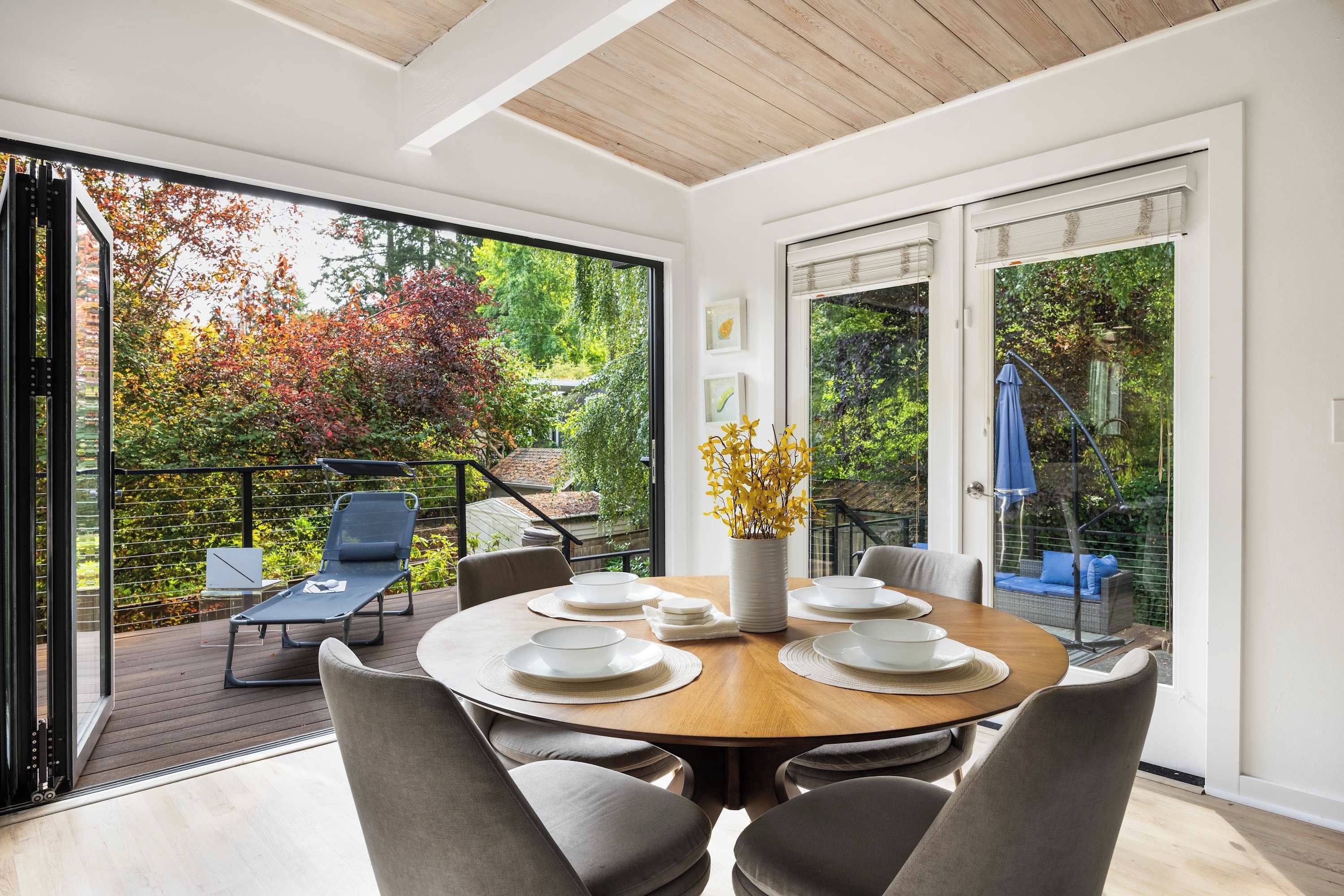 A modern dining area with a round table, chairs, and a view of a garden through large glass doors.
