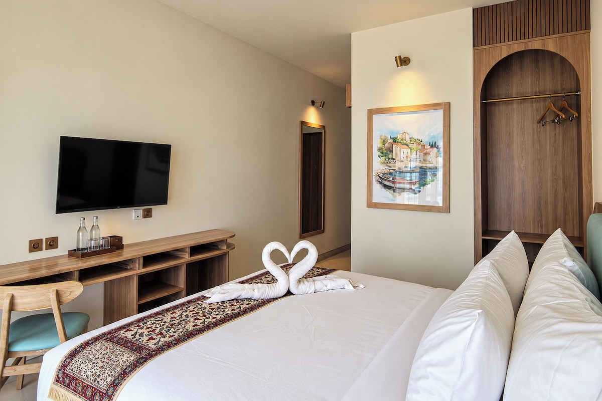 A hotel room with a bed, a television, a desk, and a painting on the wall.