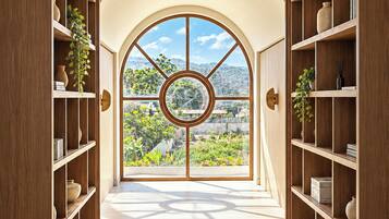 A hallway with a large arched window, wooden shelving on both sides, and a view of greenery outside.
