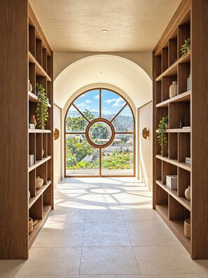 A hallway with a large arched window, wooden shelving on both sides, and a view of greenery outside.