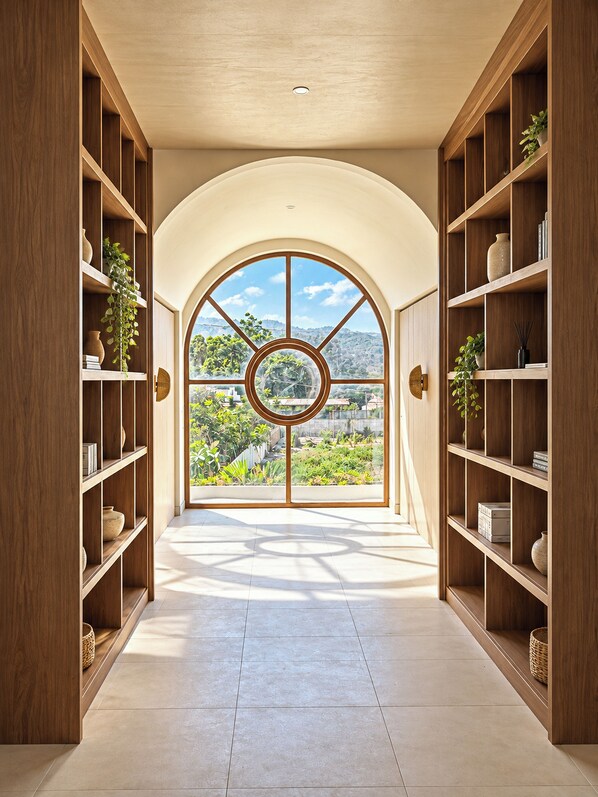 A hallway with a large arched window, wooden shelving on both sides, and a view of greenery outside.