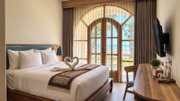 A hotel room with a bed, a wooden desk, a chair, a TV, and a window with curtains.