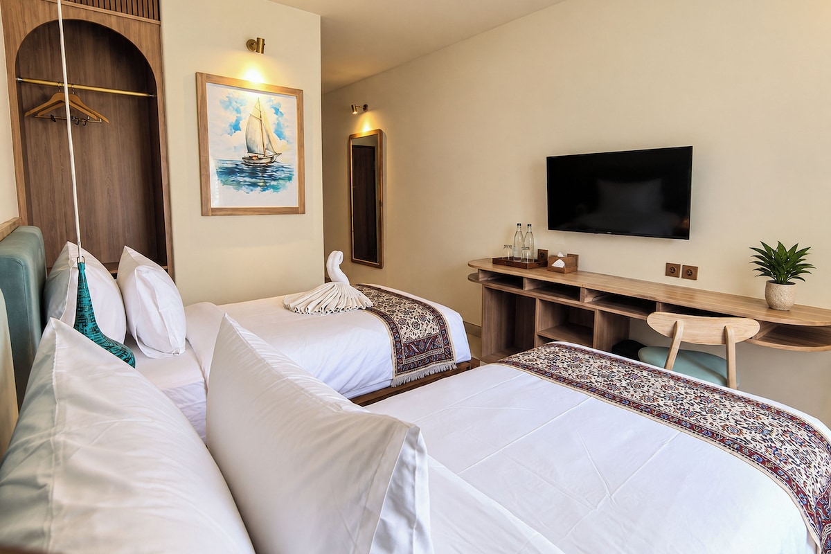 A hotel room with two beds, a desk, a television, and a mirror.