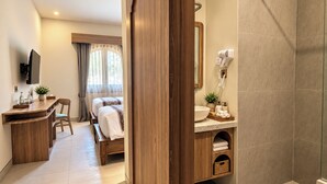 Una camera d'albergo con una scrivania in legno, un letto, un bagno con lavandino e specchio, e una cabina doccia.