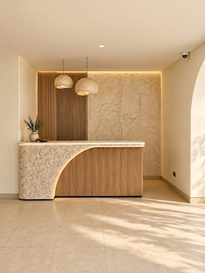 A reception desk with a wooden finish and a marble countertop. There are two pendant lights above the desk. - Laurel Davien Hotel & Resort (West Sumbawa)