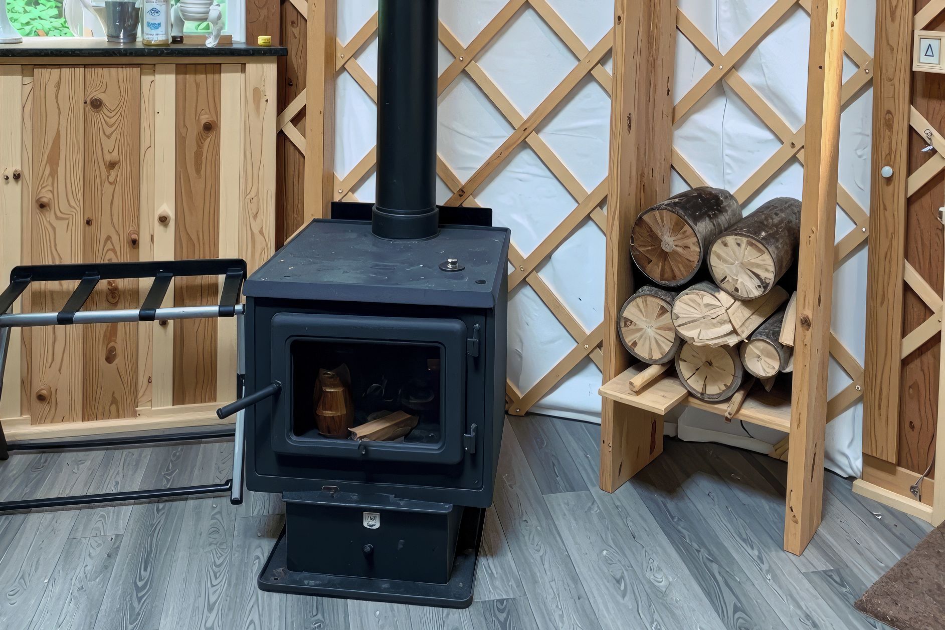 A wood-burning stove with a black exterior, a metal ladder, and a stack of firewood against a wooden lattice wall.