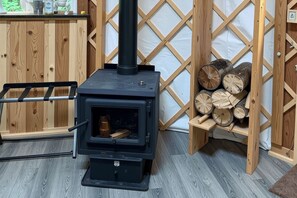 A wood-burning stove with a black exterior, a metal ladder, and a stack of firewood against a wooden lattice wall.