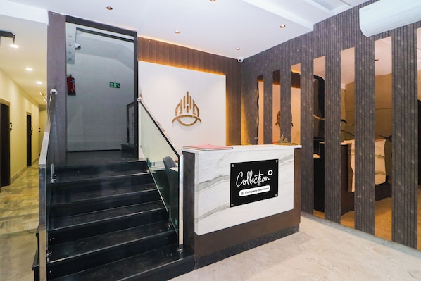 A reception desk with a sign indicating it's company-serviced, a staircase leading to an upper floor, and a fire exit sign.