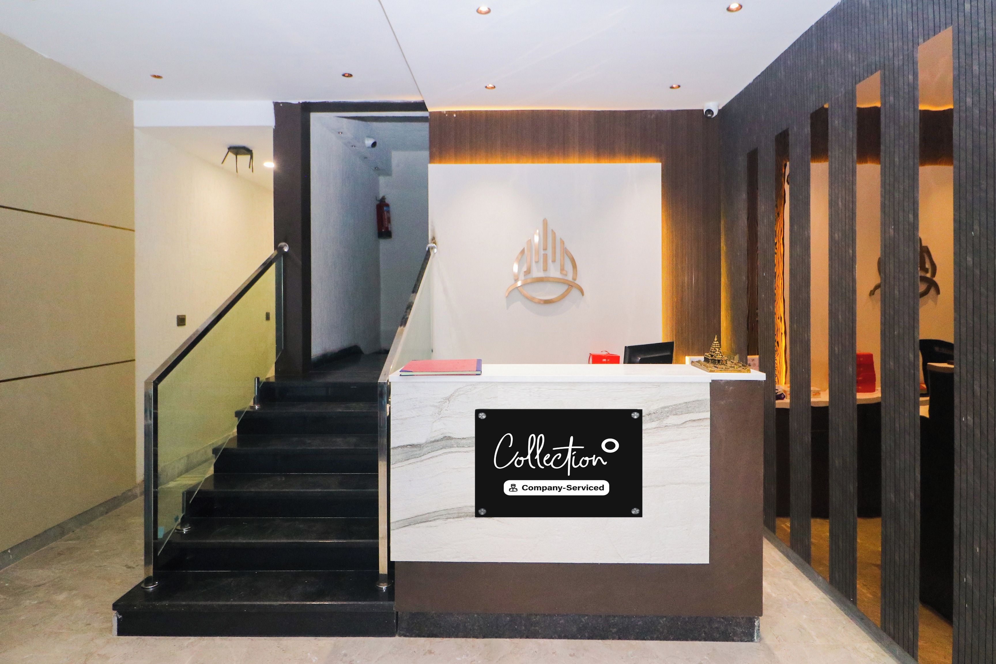 A reception desk with a marble top and a sign indicating it's company-serviced. A staircase with a metal railing leads to an upper level.