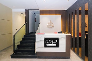 Una recepción con encimera de mármol y un cartel que indica servicio de la empresa. Una escalera con barandilla de metal conduce a un nivel superior.