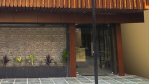A building entrance with a tiled patio, a brick wall, and a wooden overhang.