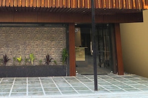 A building entrance with a tiled patio, a brick wall, and a wooden overhang.