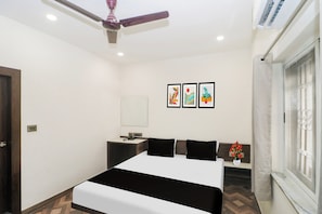 A hotel room with a bed, a desk, a chair, a window, and a ceiling fan.