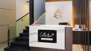 A reception desk with a sign indicating it's company-serviced, a staircase, and a decorative wall piece.