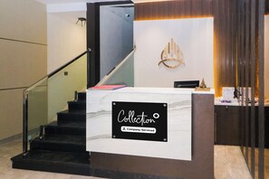 A reception desk with a sign indicating it's company-serviced, a staircase, and a decorative wall piece.