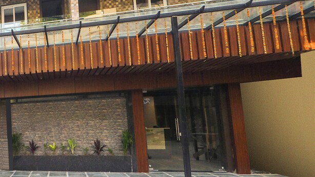 A modern building with a balcony, a glass door entrance, and a stone wall with plants.
