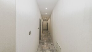 A narrow hallway with white walls and a patterned floor leading to a door at the end.