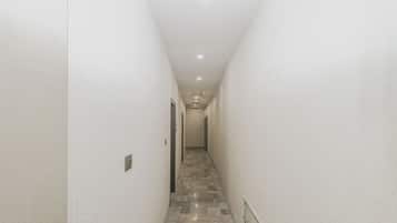 Un couloir étroit aux murs blancs et au sol à motifs, qui mène à une porte au fond.