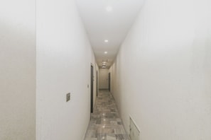 A narrow hallway with white walls and a patterned floor leading to a door at the end.