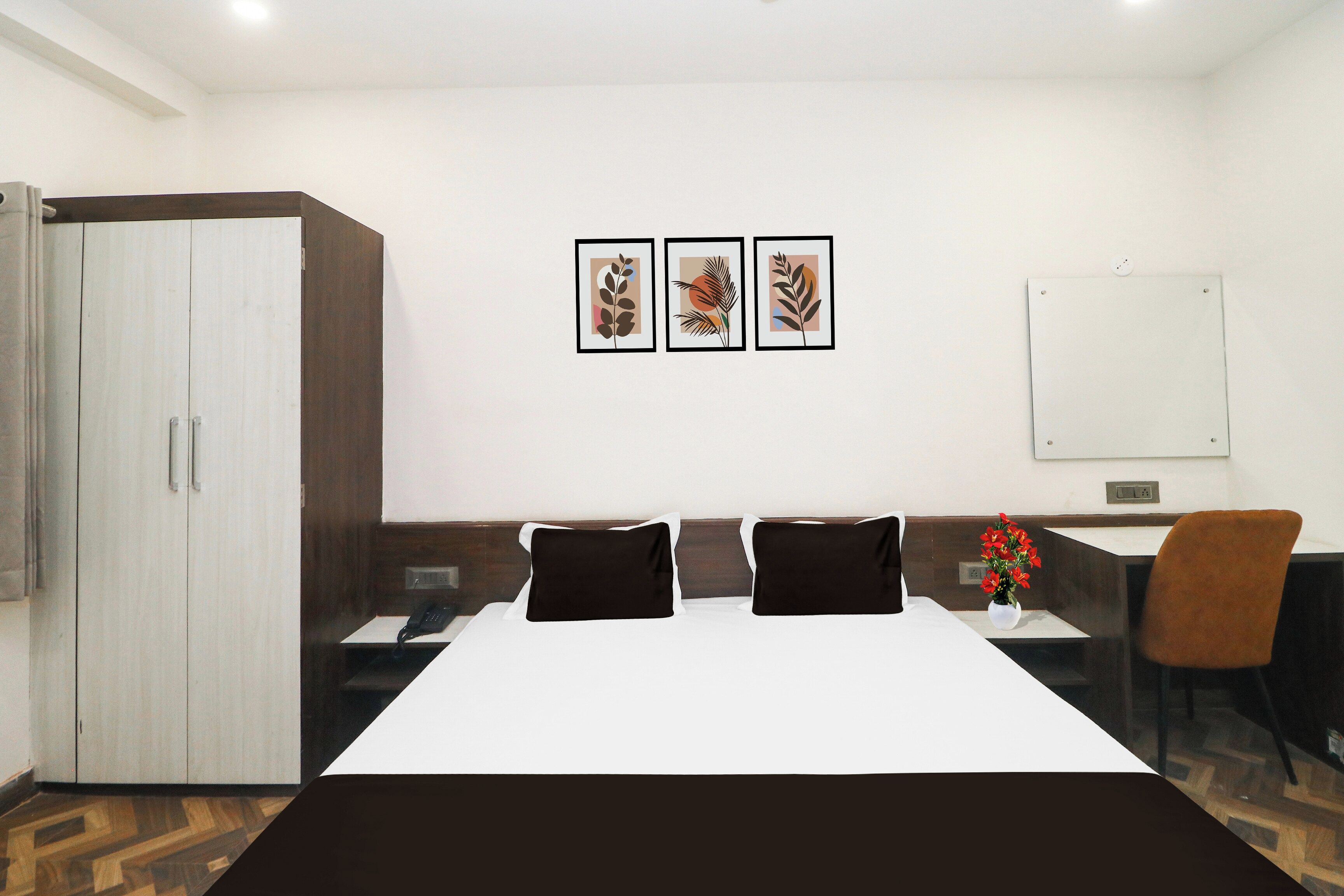 Habitación de hotel con cama, escritorio, silla, armario y tres cuadros en la pared.