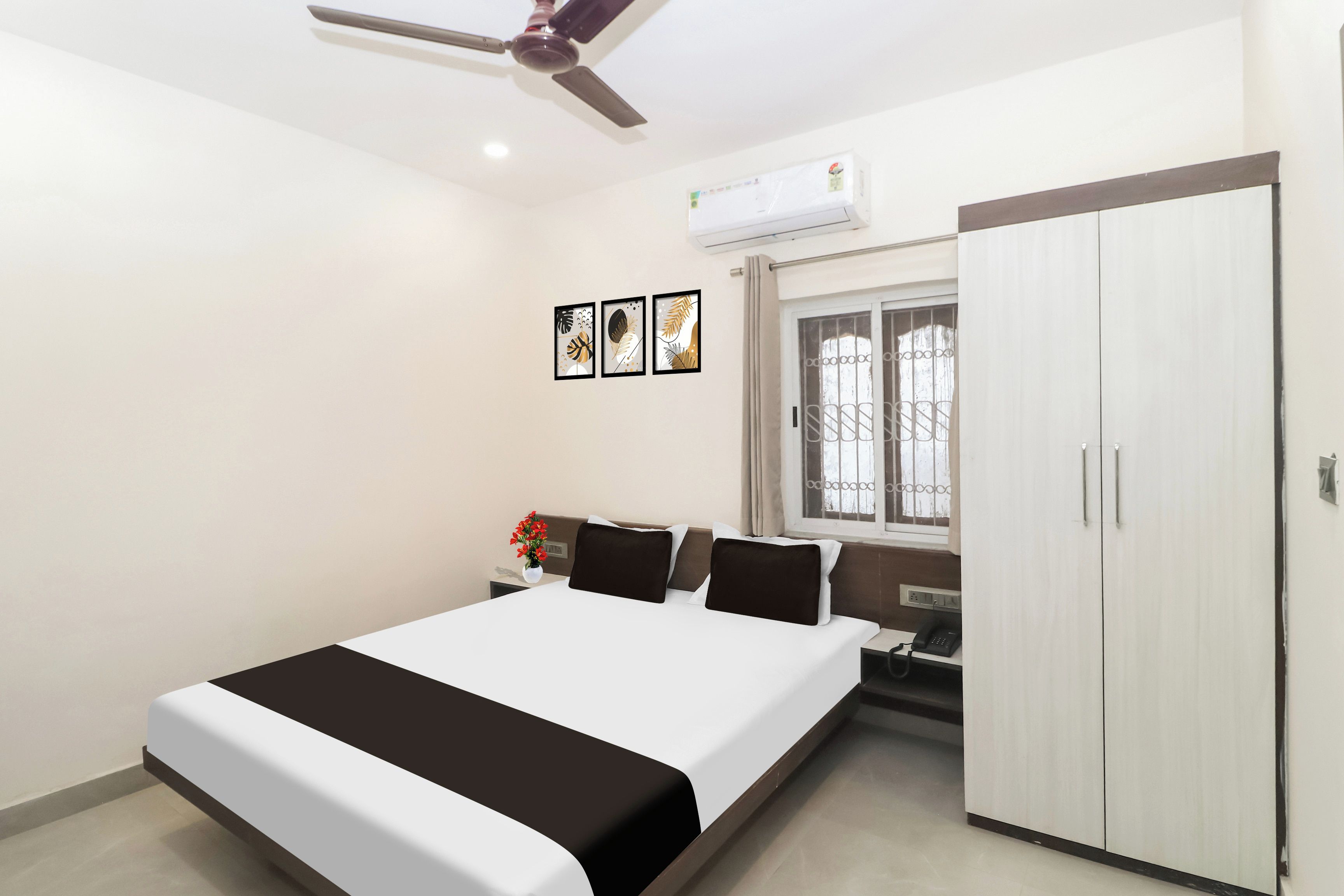 Une chambre à coucher avec un lit, une armoire, une fenêtre avec des barreaux et un ventilateur de plafond.