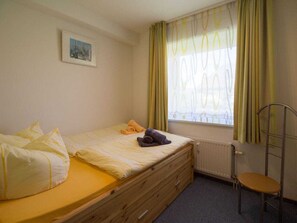 A small, single-bed room with a window, a radiator, and a chair. - Amrum / Wittdun (Wittduen)