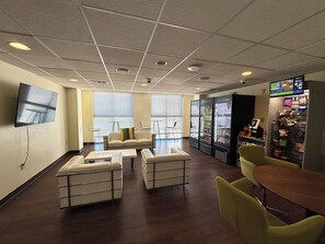 A room with a flat-screen TV mounted on the wall, a sofa, two armchairs, a small table, and a vending machine.