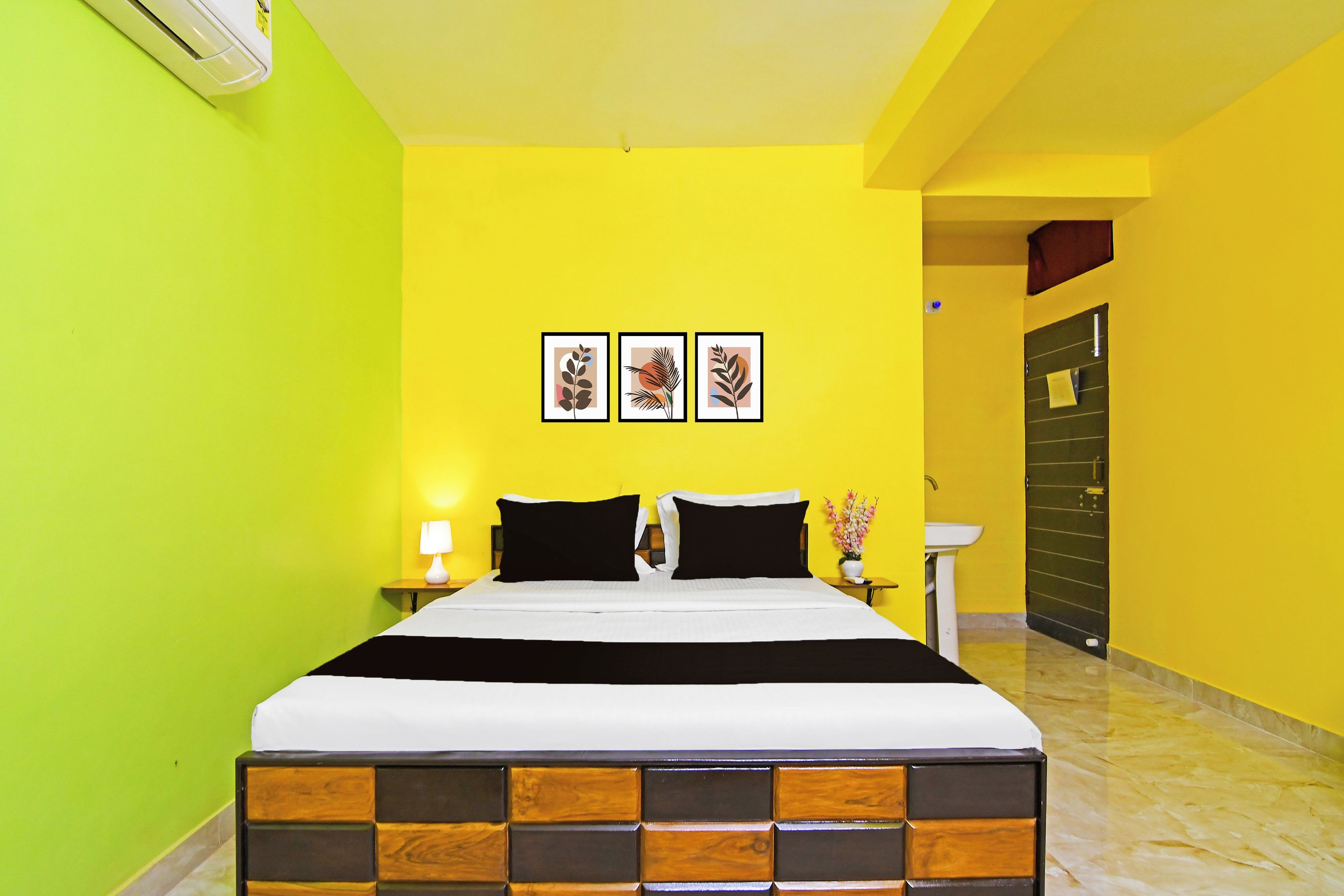 A hotel room with a bed, a nightstand, a lamp, and three framed pictures on the wall.