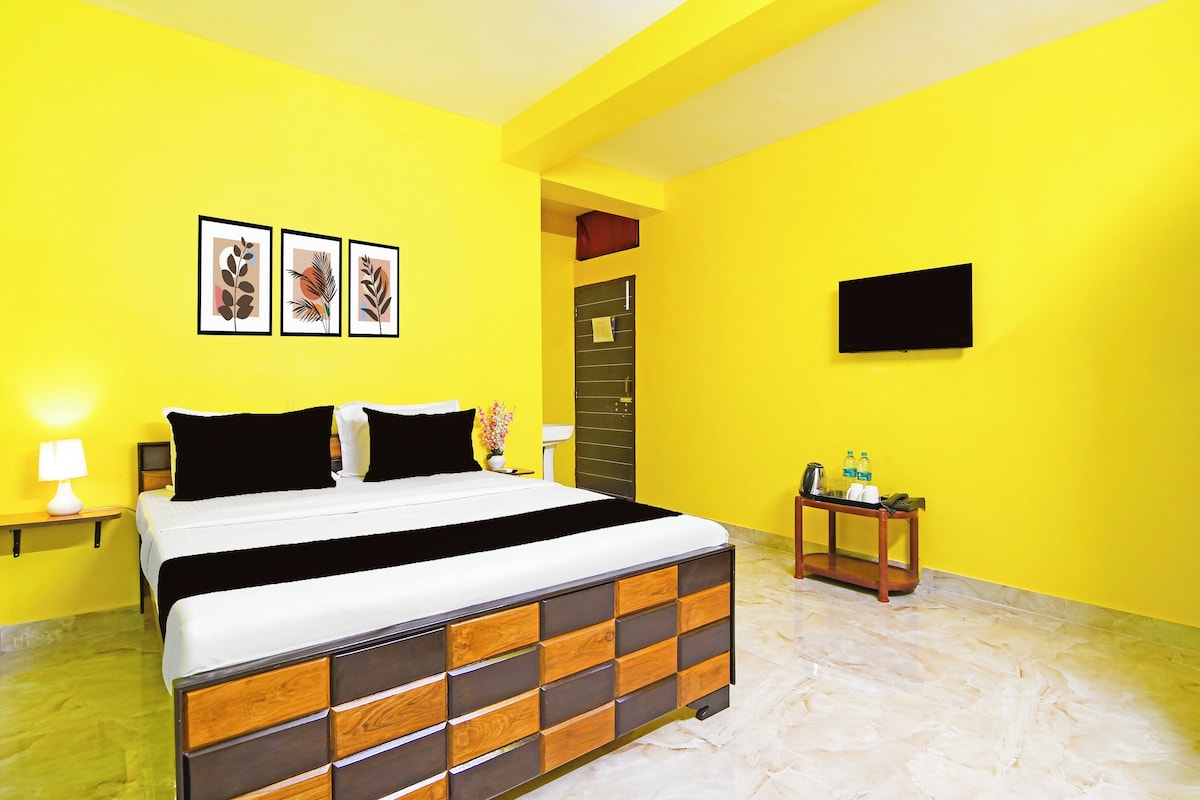 A hotel room with a bed, a bedside table, a nightstand, a wall-mounted TV, and a door.