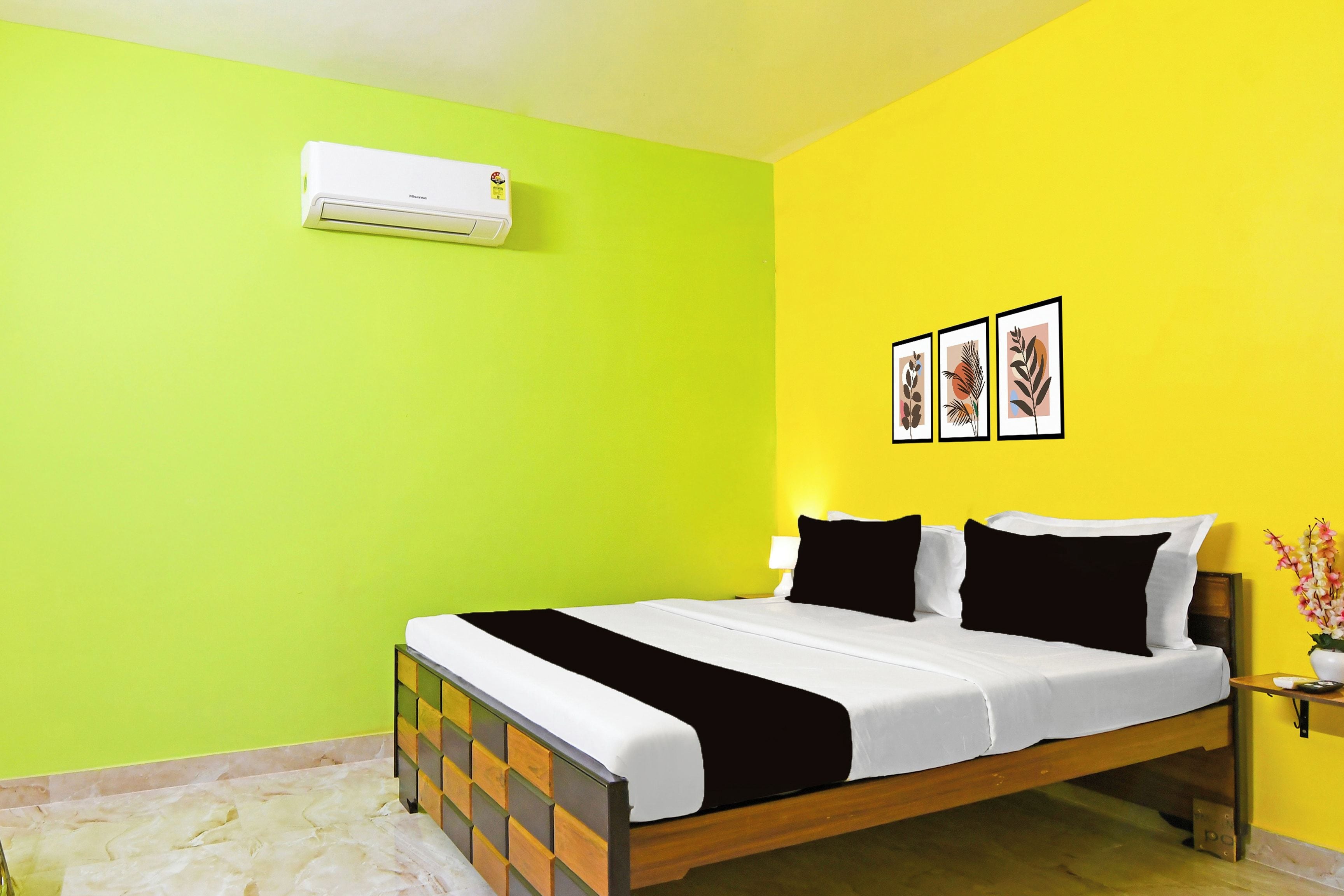 A hotel room with a bed, a nightstand, an air conditioner, and three framed pictures on the wall.