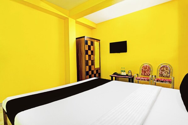 A hotel room with a large bed, a wardrobe, a desk with a chair, and a television on the wall.