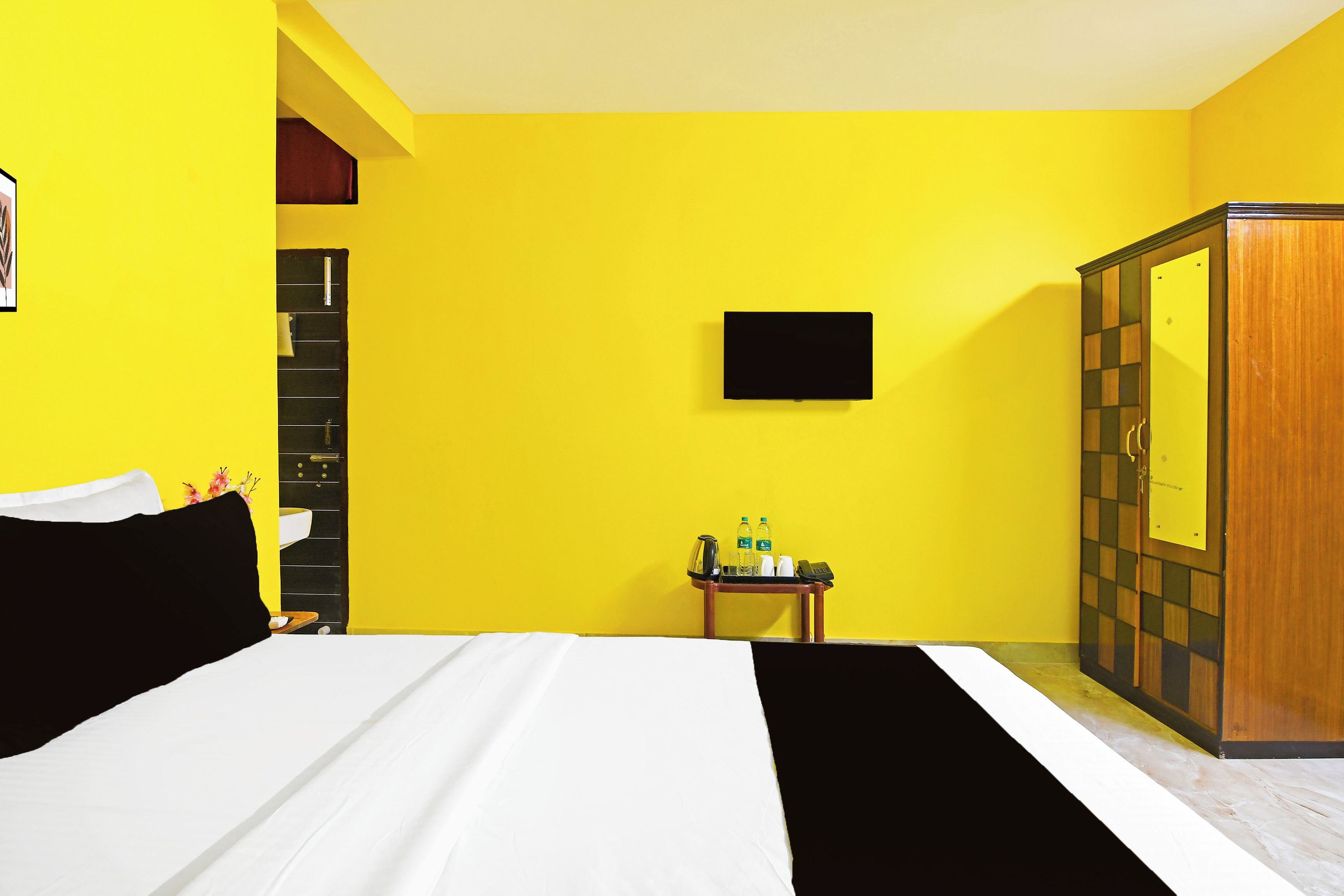 Habitación de hotel con cama, una mesita de noche con artículos de aseo, armario y televisor de pantalla plana montado en la pared.