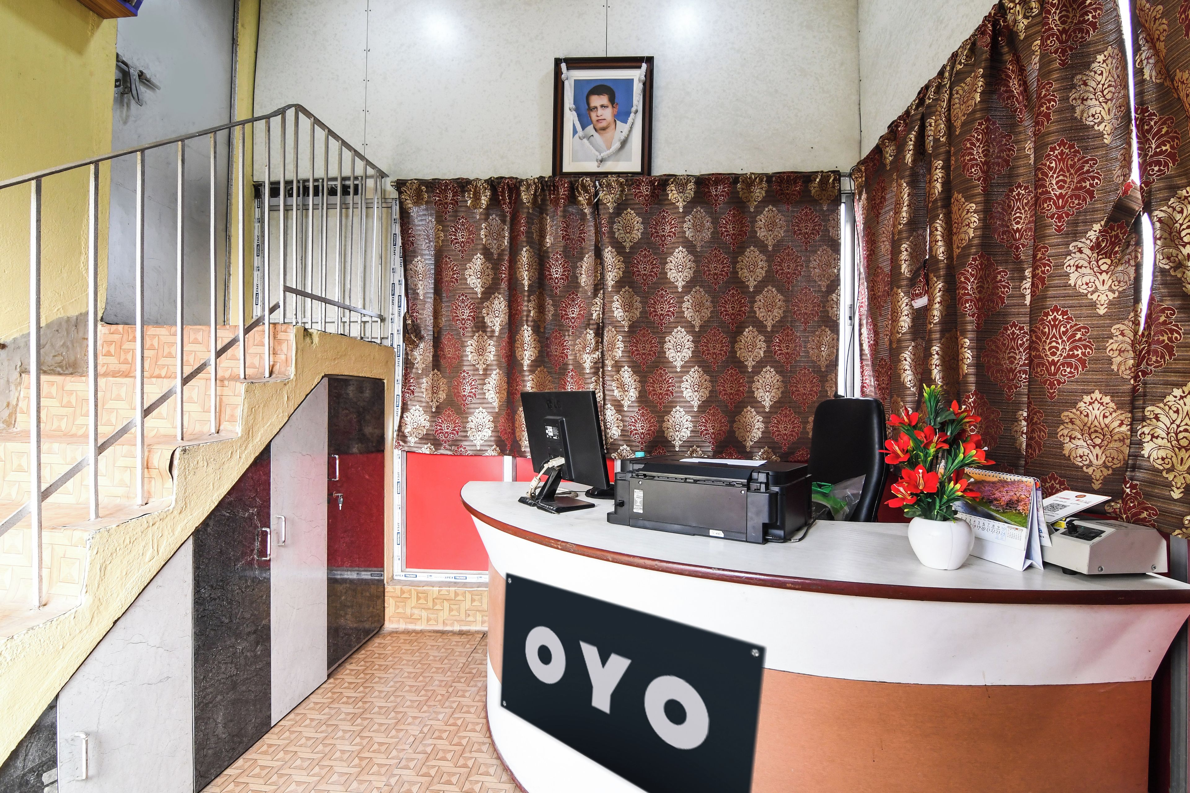 A reception desk with a sign that reads 'OYO,' a framed picture on the wall, and a staircase to the left.