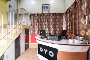 Ein Empfangsschalter mit einem Schild, auf dem 'OYO' steht, ein gerahmtes Bild an der Wand und eine Treppe zur Linken.