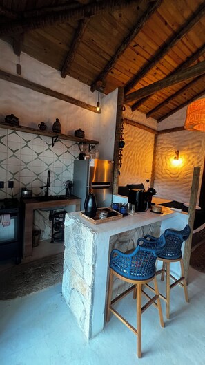 A rustic kitchen with a stone island, wooden bar stools, and a hanging light fixture.