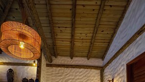 Un letto con una coperta bianca, un lampadario intrecciato sopra e un soffitto in legno rustico.