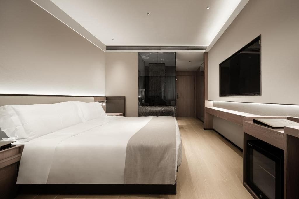A modern hotel room with a large bed, a flat-screen TV, and a built-in fireplace.