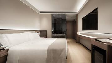 A modern hotel room with a large bed, a flat-screen TV, and a built-in fireplace.