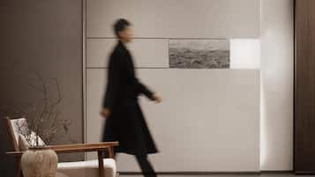 A modern interior with a wooden chair, a vase with branches, and a wall with a black and white artwork.