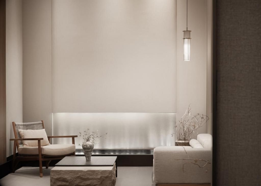Un salón minimalista con sofá, sillón, mesa de centro y un jarrón con ramas.