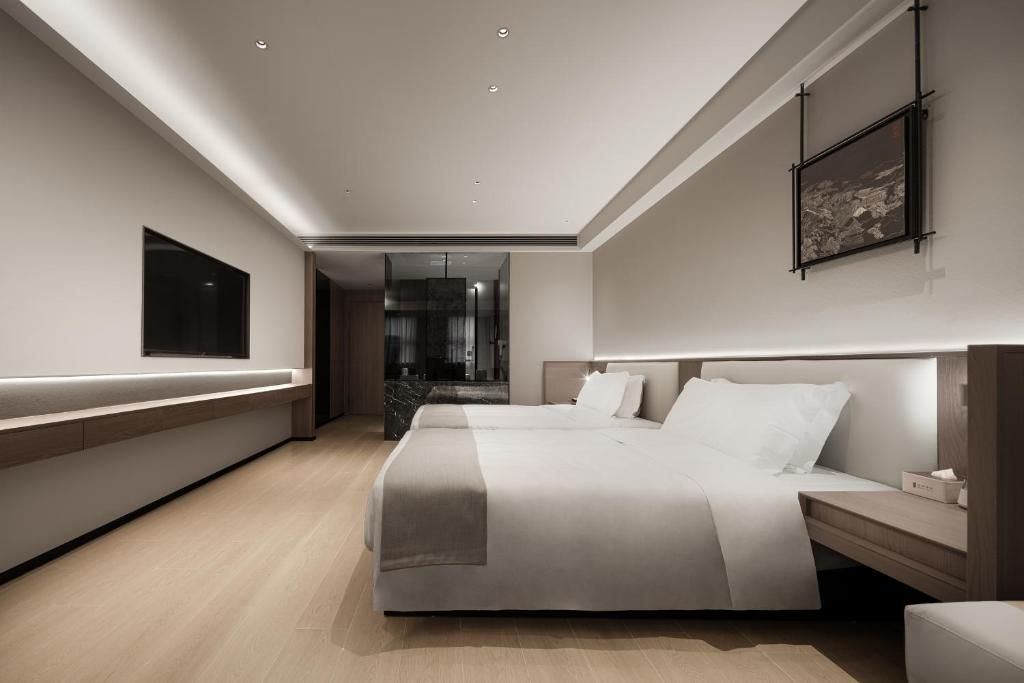 Una habitación de hotel moderna con una cama grande, mesitas de noche, un televisor de pantalla plana y vistas al baño.