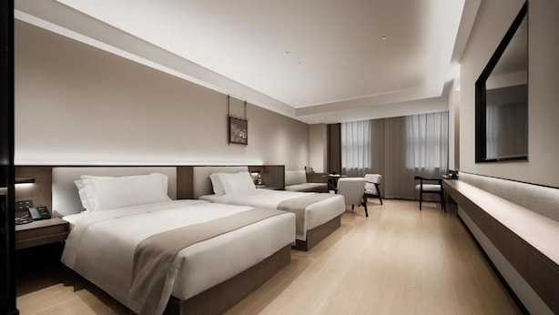 Et moderne hotelværelse med to senge, et skrivebord, en stol og et stort spejl.