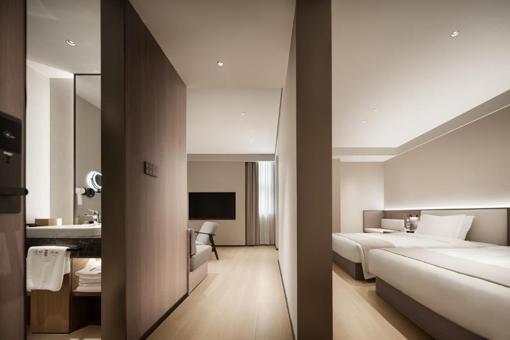 A modern hotel room with a large bed, a bedside table, a TV, and a bathroom with a mirror and sink.