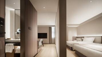 A modern hotel room with a large bed, a bedside table, a TV, and a bathroom with a mirror and sink.