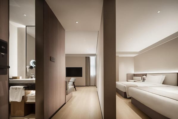 A modern hotel room with a large bed, a bedside table, a TV, and a bathroom with a mirror and sink.
