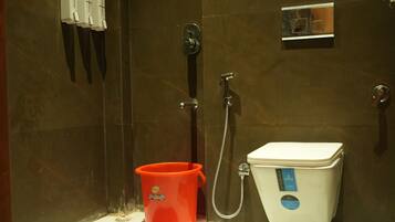 Un baño con inodoro, ducha y bidé. Hay dos dispensadores de jabón y un balde rojo en el suelo.