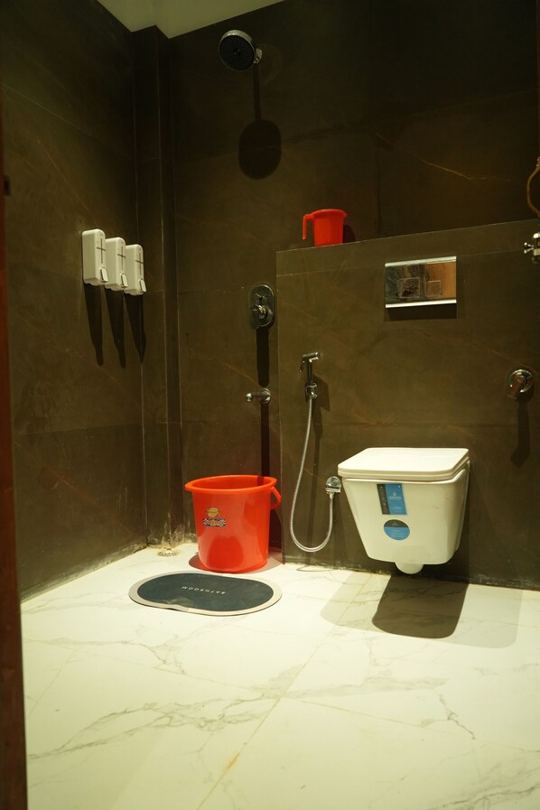 A bathroom with a toilet, a shower, and a bidet. There are two soap dispensers and a red bucket on the floor.
