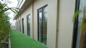 Un pasillo con piso verde artificial, ventanas amplias y fachada moderna de un edificio.