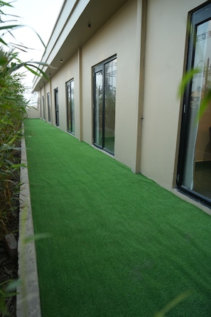 A corridor with artificial green flooring, large windows, and a modern building facade. - The Kailasha Resort (Roorkee)